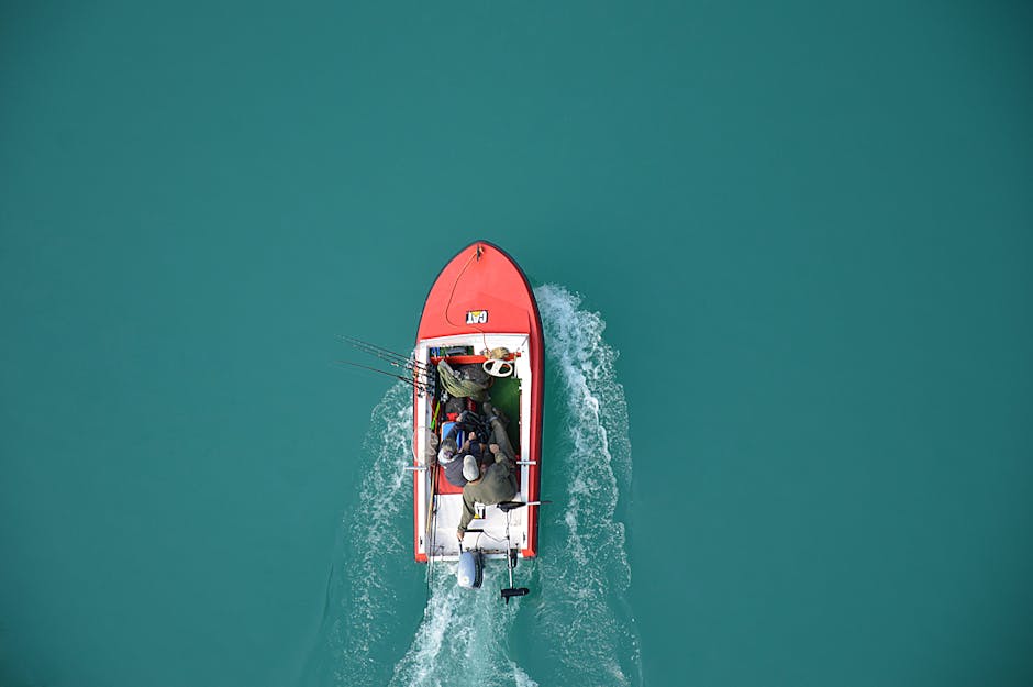 Top view of a red motorboat with fishermen navigating open turquoise waters.